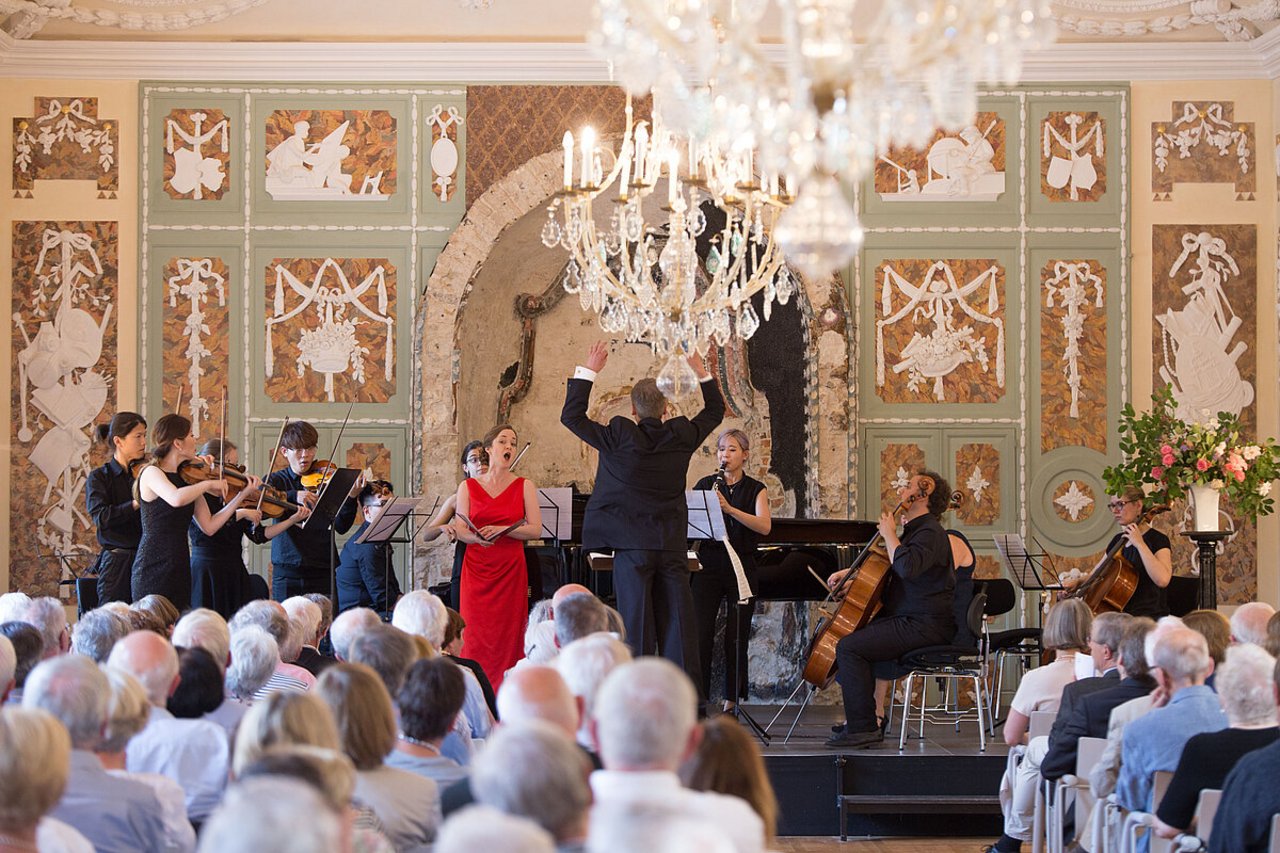 Im Konzertsaal ein Blick auf die Bühne mit Steichorchester und Sängerin im roten Kleid